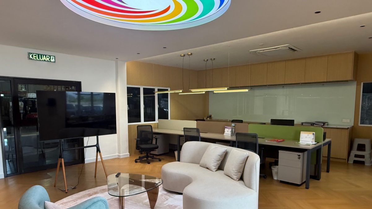 Kimagri's open-plan office: desks along one wall, a meeting area with sofas, and the Kimagri mark set into the ceiling.